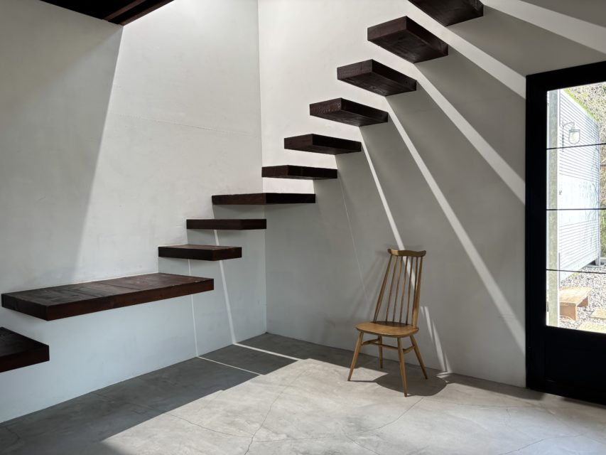 2階からLEDライトで照射し、階段の影を白壁に強く投影した撮影例。2月の低い自然光を補い、ドラマチックな陰影を作り出したスタジオ内観。